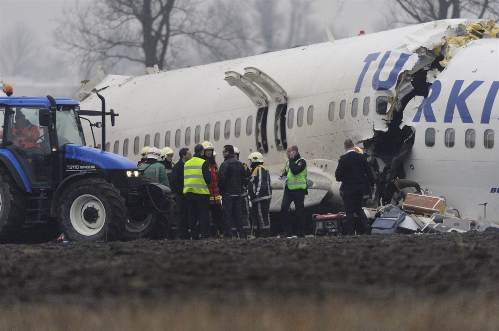 Het gebroken wrak van het Turkish Airlines-toestel in een akker, met hulpverleners in brandweerkleding en gele hesjes en een blauwe tractor ernaast.