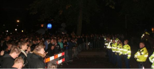 Nachtfoto van een menigte jongeren achter een afzetting, tegenover een rij agenten in gele hesjes.