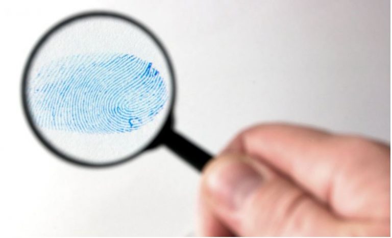 Een hand houdt een vergrootglas boven een blauwe vingerafdruk op een witte achtergrond.
