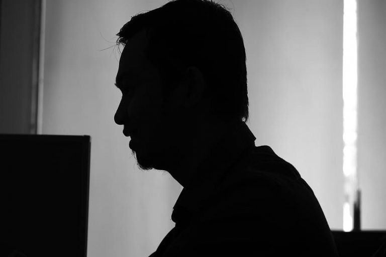 Zwart-witfoto van het silhouet van een man in profiel tegen een lichte achtergrond, naast een beeldscherm; de foto illustreert het onderwerp en laat geen herkenbaar persoon uit het artikel zien.