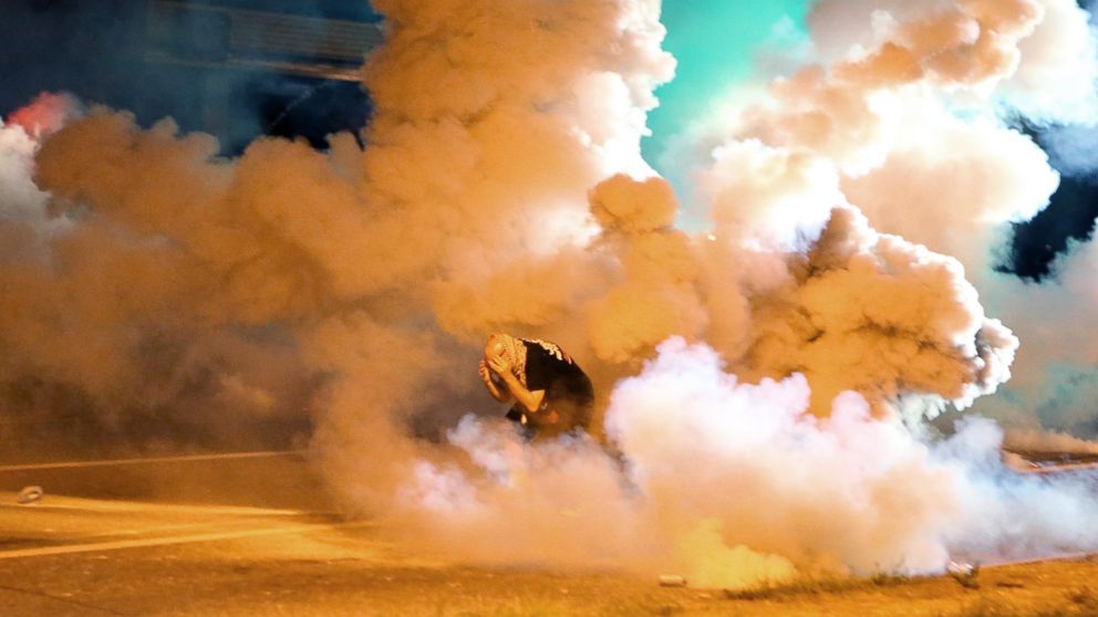 Een demonstrant duikt ineen in een grote wolk traangas op straat, ’s avonds in Ferguson.