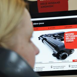 Een vrouw kijkt, onscherp op de voorgrond, naar een computerscherm met de website van Meld Misdaad Anoniem en de tekst “Moordgetuigen melden vaker” naast een foto van een pistool.