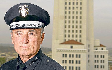 Portretfoto van Bill Bratton in politie-uniform met pet, voor een hoog wit gebouw.