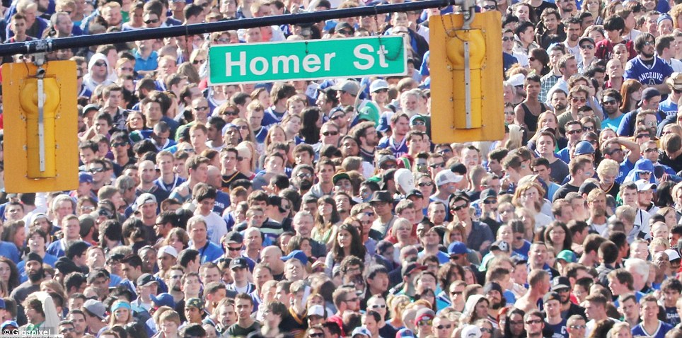 Uitsnede van de gigapixelfoto met een zee van gezichten van fans onder het straatnaambord “Homer St”, waarin individuele mensen herkenbaar zijn.