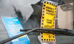Foto van een gele “Penalty Charge Notice” en een blauw parkeerkaartje achter de ruitenwisser van een geparkeerde auto.