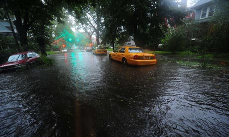 Gele taxi’s en een rode auto in een ondergelopen straat met bomen in Brooklyn tijdens orkaan Irene, in de regen.
