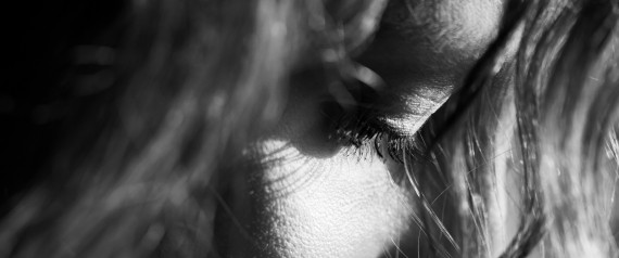 Zwart-wit close-up van het gezicht van een vrouw met neergeslagen ogen, half verborgen achter haar haar.