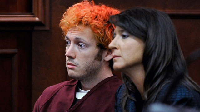 James Holmes met oranjerood geverfd haar in de rechtszaal, naast een vrouw met donker haar.
