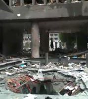 Foto van de verwoeste ingang van een regeringsgebouw in Oslo na de bomaanslag, met puin en een krater in de grond.