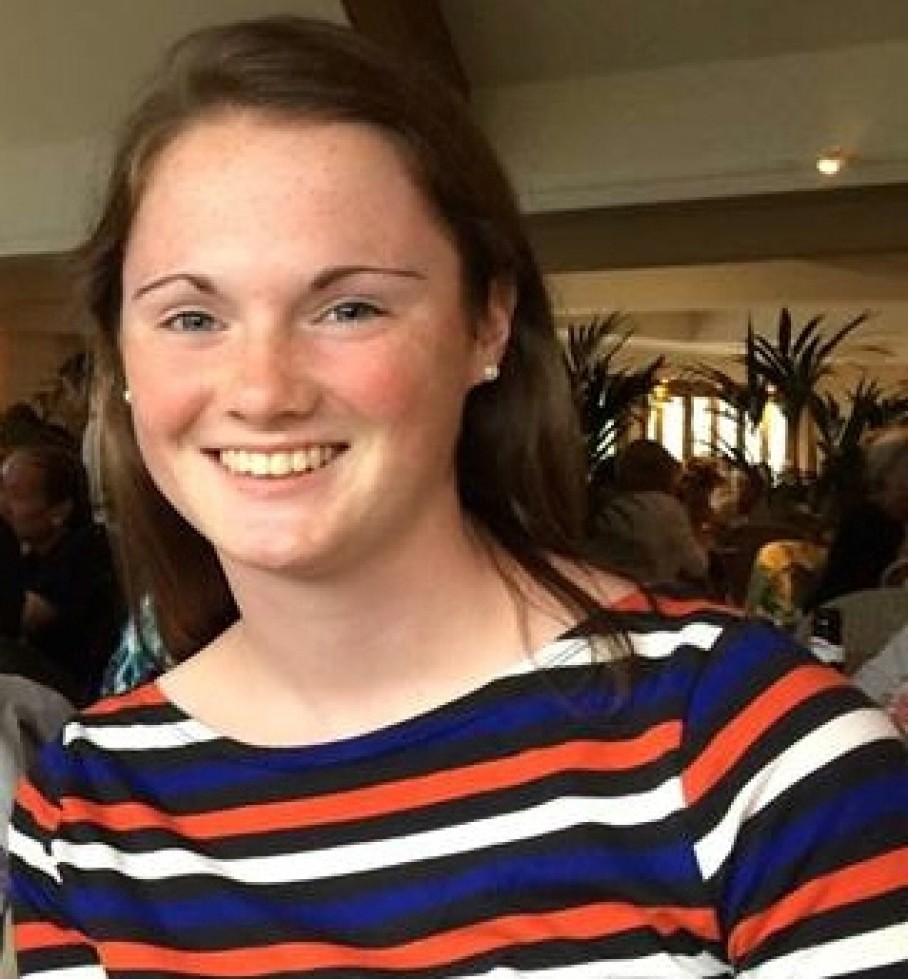 Portret van Hannah Graham, lachend, met lang bruin haar en een gestreept shirt in blauw, oranje en wit.
