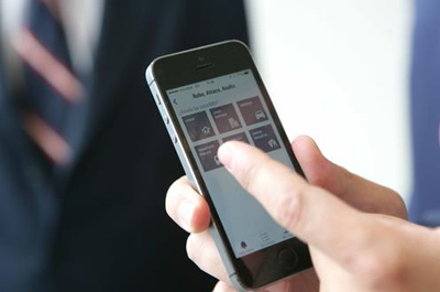 Een hand tikt op een iPhone waarop de AlertCops-app geopend is, met een man in pak wazig op de achtergrond.