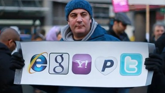 Een demonstrant houdt een bord omhoog met de logo’s van Internet Explorer, Google, Yahoo, PayPal en Twitter.
