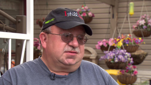 Steve Huckins, een man met pet en bril, wordt geïnterviewd voor een veranda met hangende bloembakken.