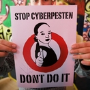 Handen houden een poster omhoog met de tekst “Stop cyberpesten – Don’t do it” en een getekend meisje met een telefoon, doorgestreept met een rode cirkel.