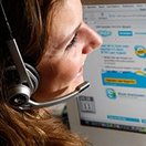 Een vrouw met een headset kijkt naar een computerscherm met een geopende website.