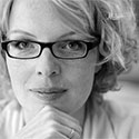Zwart-wit portret van Beatrice de Graaf, een vrouw met krullend blond haar en een donkere bril die met haar kin op haar hand rust.