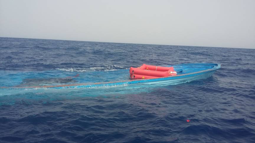 Een half gezonken blauwe houten boot met oranje reddingsvlotten op een woelige blauwe zee.