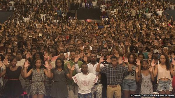 Een grote zaal vol studenten staat met de handen omhoog in het gebaar “Hands up, don’t shoot”. Rechtsonder staat “Howard Student Association”.