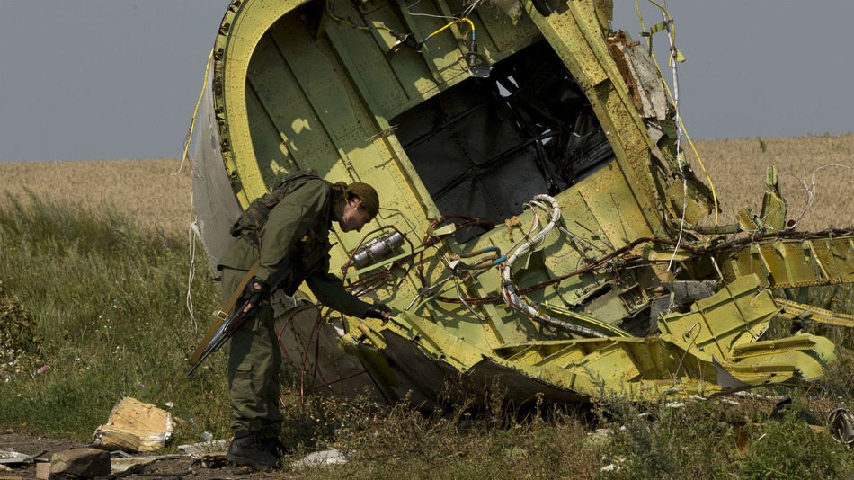 Een gewapende man in camouflagekleding buigt zich over een groot stuk wrakdeel van vlucht MH17 in een graanveld in Oekraïne.