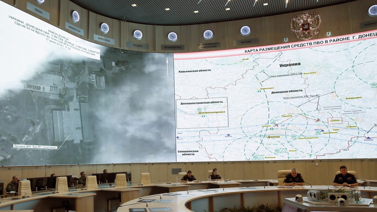 Persbriefing van het Russische ministerie van Defensie: militairen zitten aan een halfronde tafel voor grote schermen met een satellietbeeld en een Russischtalige kaart van luchtafweermiddelen rond Donetsk.