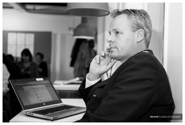 Zwart-witfoto van Frank Smilda die aandachtig luistert achter een laptop, met de hand aan zijn kin.