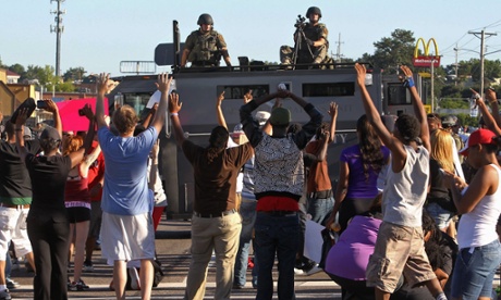 Demonstranten in Ferguson steken hun handen omhoog voor een gepantserd politievoertuig waarop zwaarbewapende agenten staan.