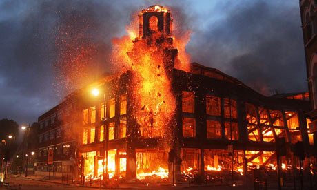 Foto van een groot gebouw dat in lichterlaaie staat in Tottenham, met vlammen uit de ramen en het torentje.