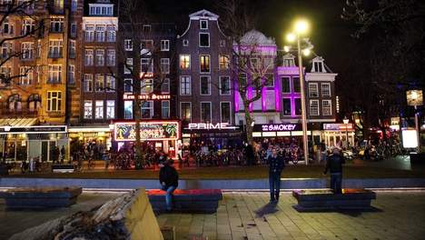 Een uitgaansplein bij avond, met verlichte gevels, cafés en voorbijgangers.