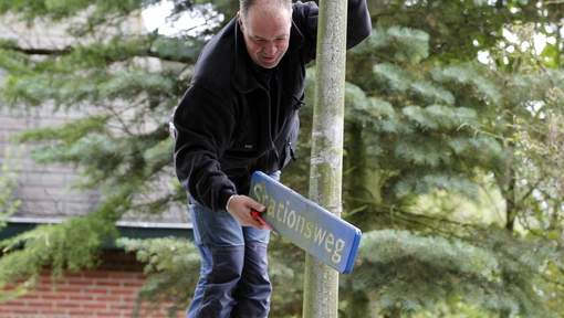 Een man haalt het straatnaambord “Stationsweg” van een paal.