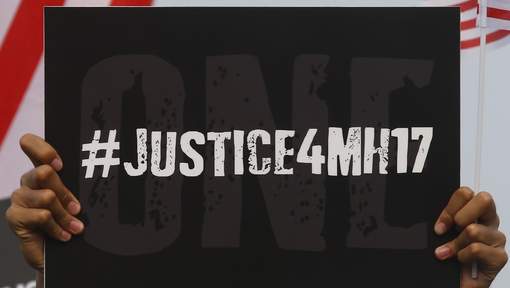 Twee handen houden een zwart bord omhoog met in witte letters de hashtag #JUSTICE4MH17.