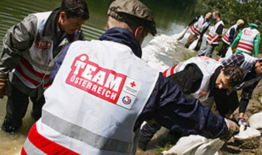 Helpers in hesjes van “Team Österreich” van het Oostenrijkse Rode Kruis leggen zandzakken langs het water.