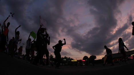 Silhouetten van demonstranten met geheven vuisten en borden tegen een paarse avondlucht in Ferguson.