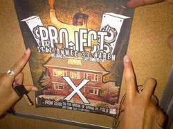 Twee handen hangen een Project X-poster met een grote X en een getekend huis op een prikbord.