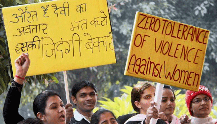 Demonstranten in India houden gele borden omhoog, waarvan één met de tekst “Zero tolerance of violence against women” en één met Hindi-tekst.