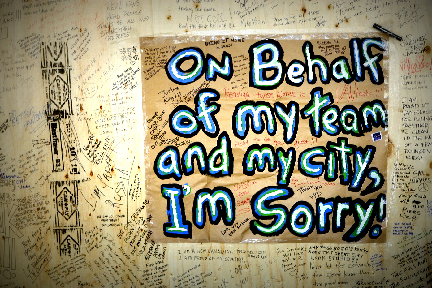 Een met boodschappen volgeschreven houten schot met in het midden een bord met de tekst “On behalf of my team and my city, I’m sorry!” in blauwe, groene en witte letters.