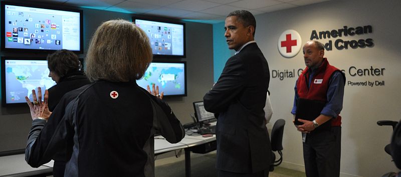 Volgens de bestandsnaam president Obama op bezoek bij het digitale centrum van het Amerikaanse Rode Kruis, waar medewerkers bij een wand met beeldschermen vol kaarten en grafieken staan.