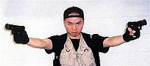 Cho Seung-Hui met pet en een vest met zakken richt met gestrekte armen twee pistolen naar voren.
