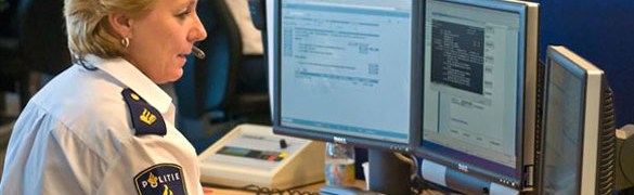 Een politiemedewerker met headset zit in een meldkamer achter meerdere computerschermen.