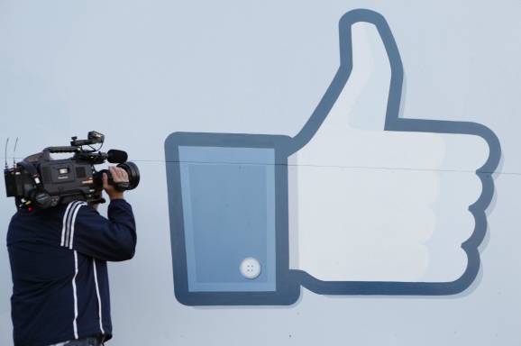 Een cameraman filmt voor een grote muurafbeelding van de Facebook-duim omhoog, het “vind ik leuk”-symbool.