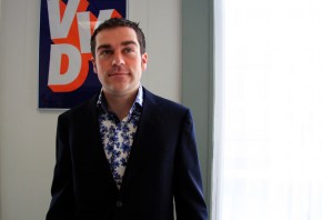 Klaas Dijkhoff in een donker colbert en een bloemetjesoverhemd, voor een VVD-poster aan de muur.