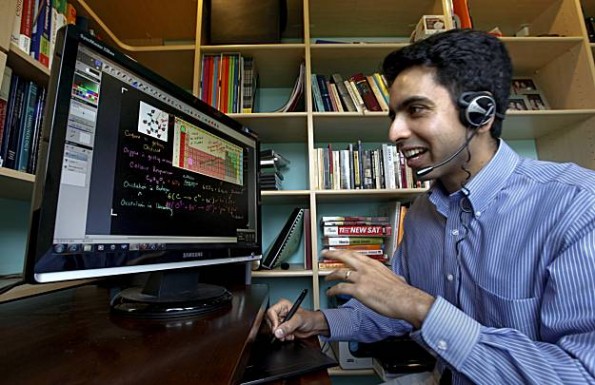 Een lachende man met headset tekent met een pen op een tekentablet, terwijl op zijn beeldscherm een scheikundeles met formules staat. Op de achtergrond boekenkasten.