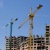 Bouwkranen boven flatgebouwen in aanbouw tegen een blauwe lucht.