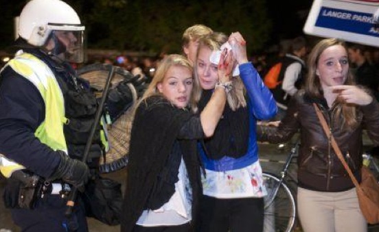 Geschrokken jonge vrouwen lopen tijdens de rellen in Haren langs een agent van de ME; een van hen houdt een bebloede doek tegen haar hoofd.