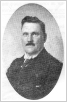 Ovaal zwart-wit portret van de Hilversumse politiecommissaris A.L. van Beusekom, een man met snor in een donker pak.