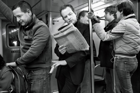 Zwart-witfoto van Martin Schoeller bij het artikel over Apollo Robbins in The New Yorker: in een volle metro reikt een man met een krant ongemerkt naar de tas van een medereiziger.