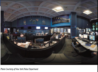 Panoramafoto van het Real Time Crime Center in New York, met werkplekken vol beeldschermen en een grote videowand; het bijschrift luidt “Photo Courtesy of New York Police Department”.