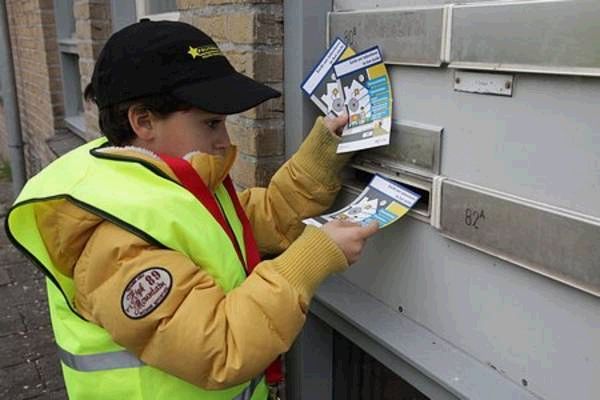 Een jongen met pet en geel hesje stopt folders in de brievenbussen van een portiek.