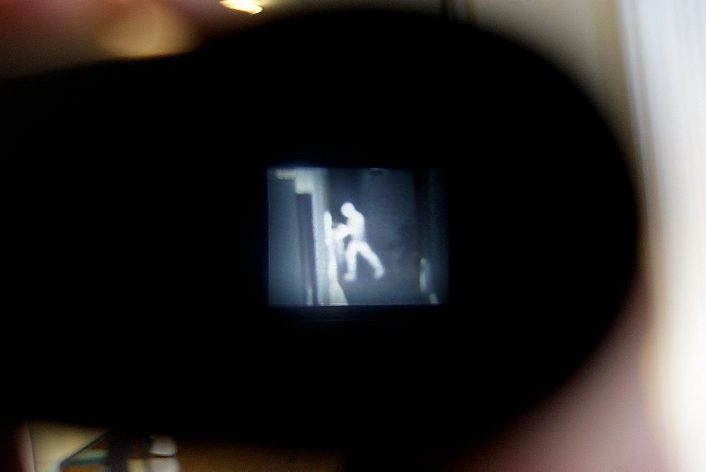 Zoeker van een videocamera met een korrelig, lichtgevend nachtbeeld van een persoon bij een deur, mogelijk een inbreker.