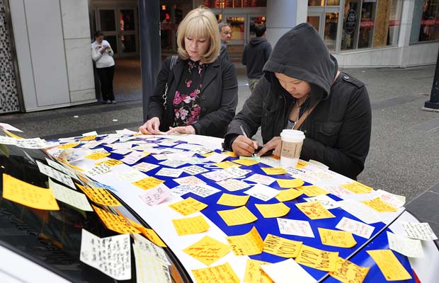 Twee vrouwen schrijven briefjes op een politieauto die al bijna helemaal bedekt is met gele en witte post-its.